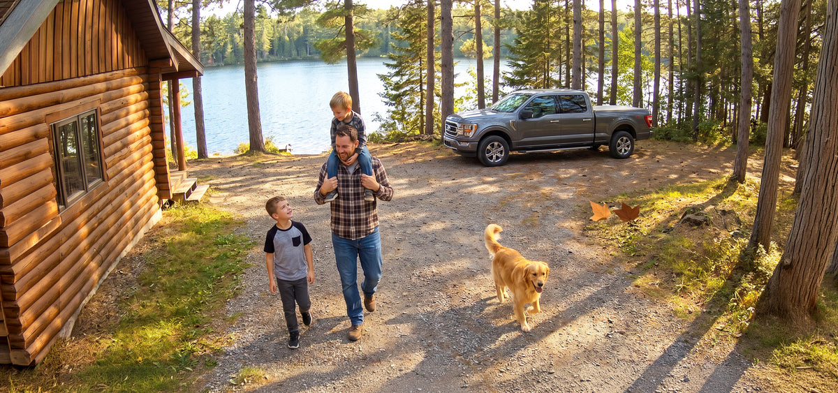 A family, pickup truck, dog, and chicken outside a lakeside cabin